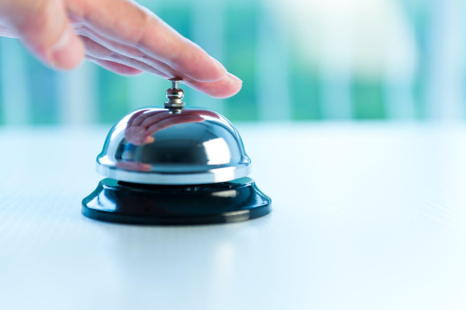 A hand about to ring a reception desk bell