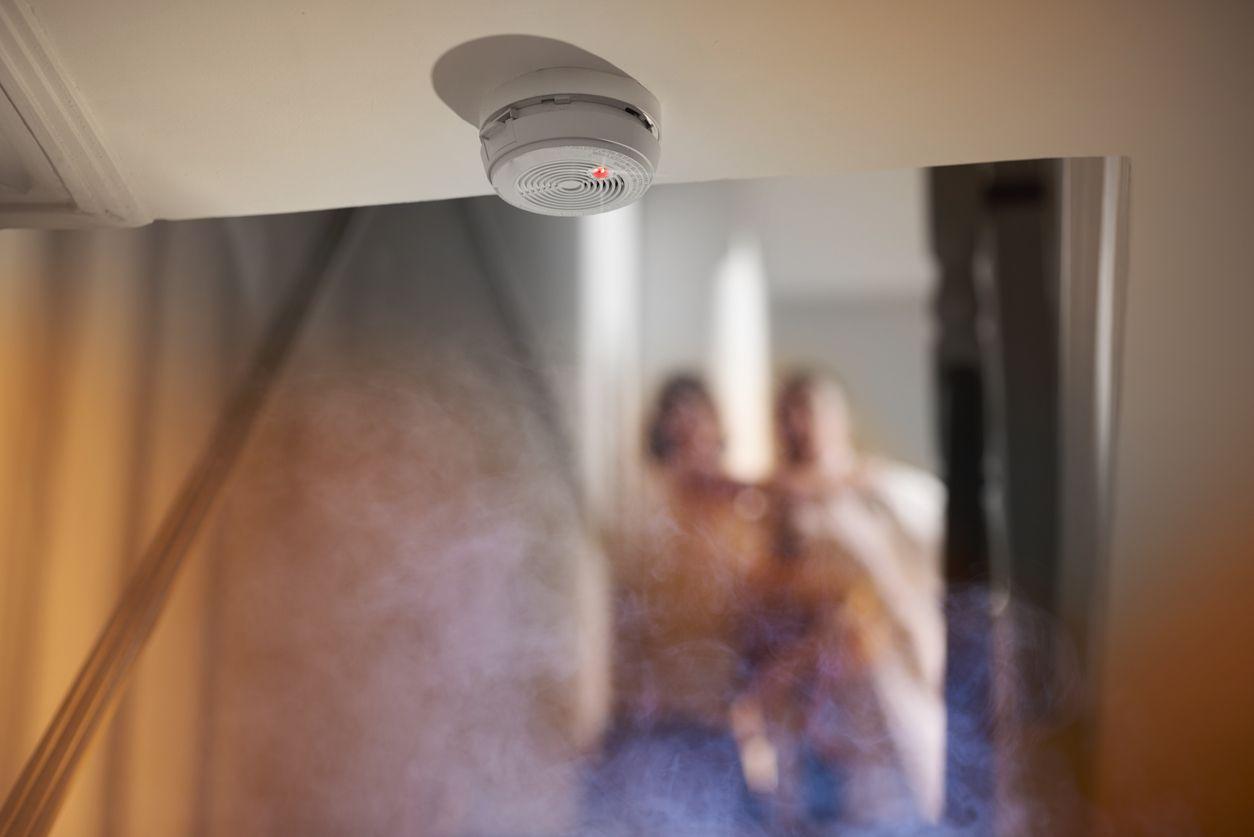 A smoke alarm on a ceiling as smoke fills the room