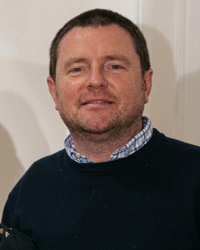 Stuart Leonard, smiling, in a navy jumper and checked shirt